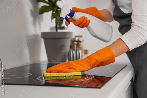 Female janitor cleaning electric stove in kitchen, closeup photo