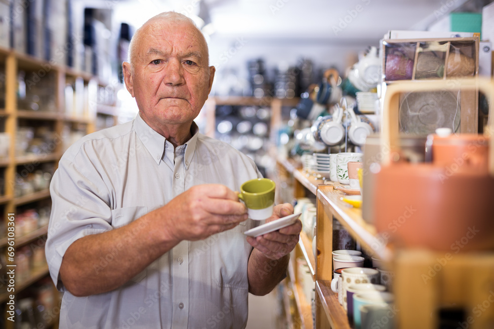 Elderly male customer chooses plates and cups in tableware store