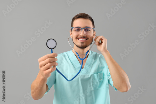Young doctor in eyeglasses with stethoscope on grey background