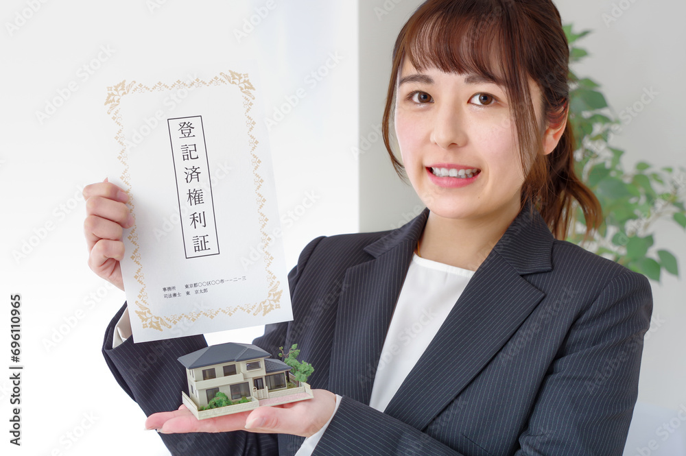 不動産の権利書と住宅模型を持つ女性 不動産の権利書と住宅模型を持つ女性