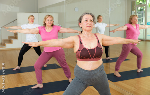 Three European ladies are doing warrior II pose beside a mirror