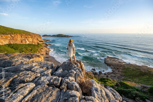 Young woman standing on a rock above the sea in the evening light, beach at The Gap, Robberg Peninsula hiking trail, Garden Route, Robberg Peninsula, Plettenberg Bay, Western Cape, South Africa photo