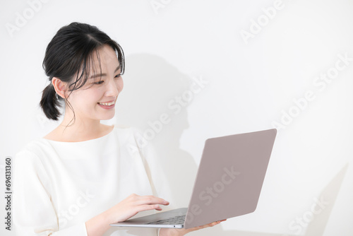 笑顔でノートパソコンを見るオフィスカジュアルの若い女性 白バックの上半身 右にコピースペースあり