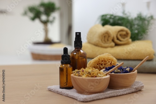 Bottles of essential oils  bowls with dry flowers and natural sponge on light wooden table  space for text. Spa therapy