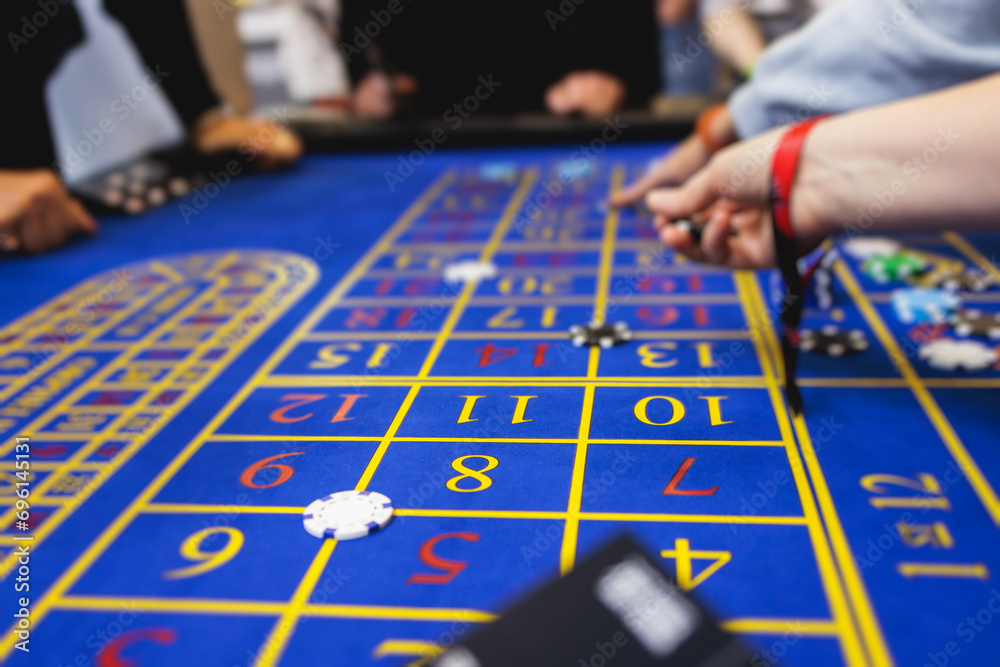 Vibrant casino table with roulette in motion, with casino chips, tokens, the hand of croupier, dollar money and a group of gambling rich people playing bet, blue poker table and deck of cards Vibrant casino table with roulette in motion, with casino chips, tokens, the hand of croupier, dollar money and a group of gambling rich people playing bet, blue poker table and deck of cards