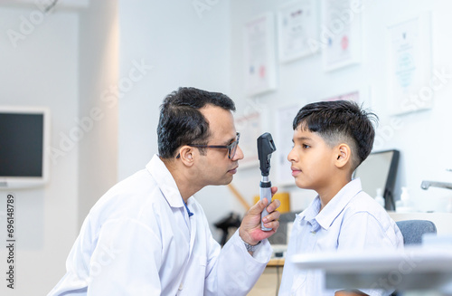 Optometrist doing sight testing for child patient in clinic  Indian child choosing eyeglasses in optics store  Boy doing eye test checking examination with optometrist in optical shop