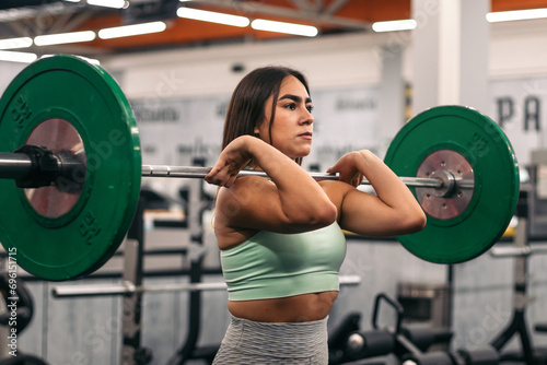 concentrated female athlete lifting barbell during weightlifting workout in gym while looking away