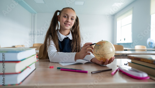 Caucasian schoolgirl sits at her desk at school and studies the globe. 