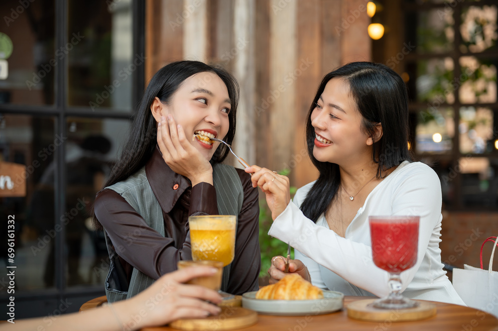 A lovely Asian girl is feeding food to her female friend, enjoying eating food at a cafe together.
