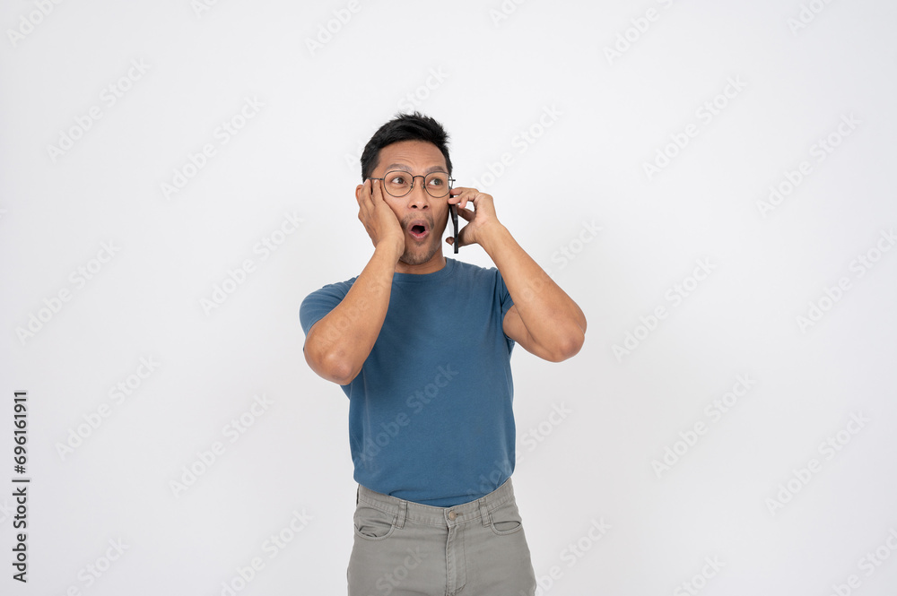A surprised, shocked Asian man is talking on the phone with someone, isolated background. A surprised, shocked Asian man is talking on the phone with someone, isolated background.