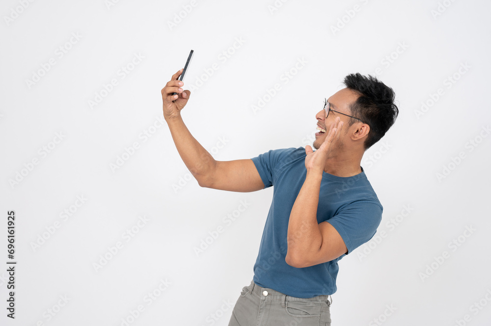 A cheerful Asian man is enjoying talking with his friend on his smartphone, waving hand to say hello