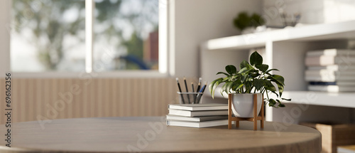 An empty space on a hardwood table with a potted plant, books, and a pencil stand in a modern room.