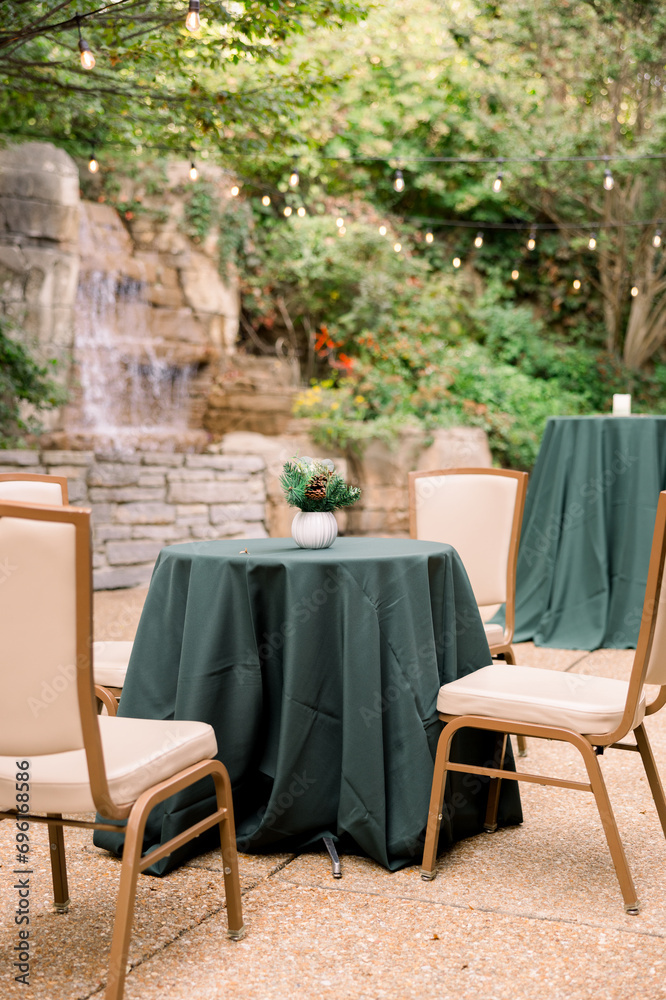 A table is set up outside by a waterfall with green tablecloth and chairs surrounding it. 
