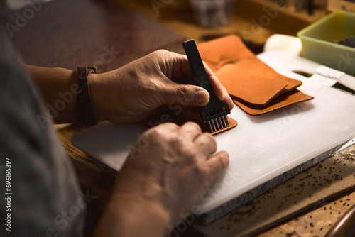 man learning to work with leather stitching punch, close up cropped side view photo. focus on sewing tool and arms, hands photo