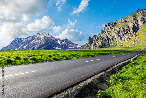 Asphalt highway and green meadows with mountain natural landscape under the blue sky photo