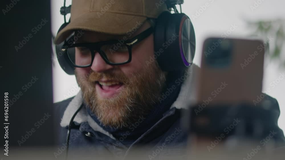 Close up of Caucasian musician in headphones playing MIDI keyboard, creates music and moves rhythmically sitting in gazebo in forest. Adult man uses laptop and phone on tripod to record song outdoors. Close up of Caucasian musician in headphones playing MIDI keyboard, creates music and moves rhythmically sitting in gazebo in forest. Adult man uses laptop and phone on tripod to record song outdoors.