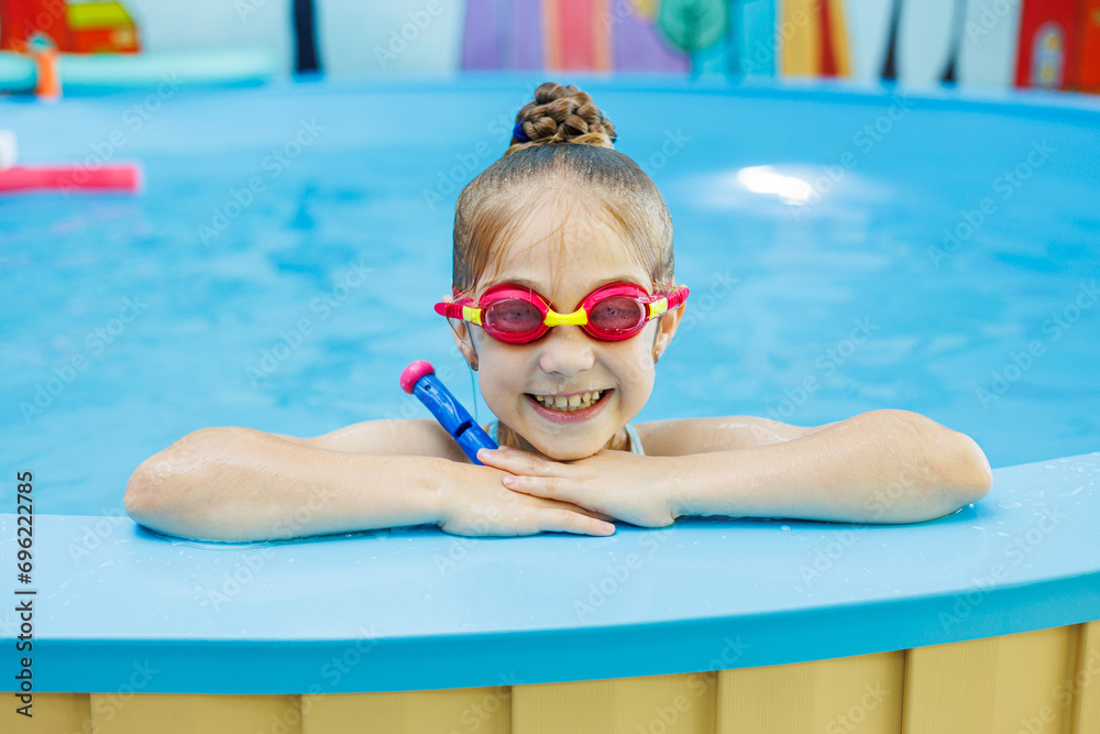 A little girl of 7 years swims in the pool. The girl is sitting in the pool in swimming goggles.