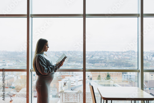 Young pregnant woman at work in the office standing near the window. Work during pregnancy. Pregnant business lady © Дмитрий Ткачук
