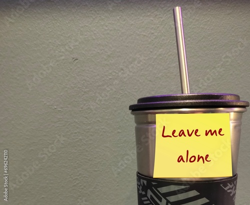 Tumbler with yellow stick note written LEAVE ME ALONE on copy space wall - refrain from disturbing, interfering or need private time - asking other to stop bothering or go away