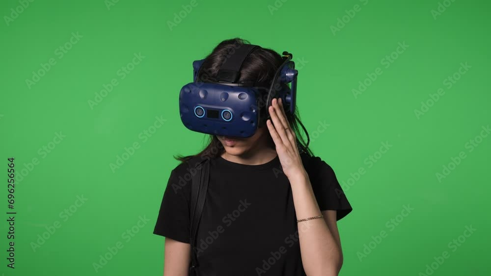 Portrait of a young woman in a virtual reality headset in a studio on a green background, she looks around emotionally in the virtual world. Chromakey. 3D glasses. Portrait of a young woman in a virtual reality headset in a studio on a green background, she looks around emotionally in the virtual world. Chromakey. 3D glasses.