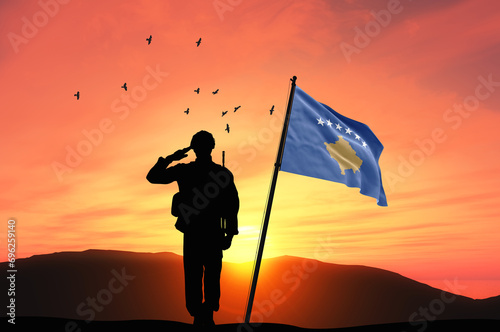 Silhouette of a soldier with the Kosovo flag stands against the background of a sunset or sunrise. Concept of national holidays. Commemoration Day. photo
