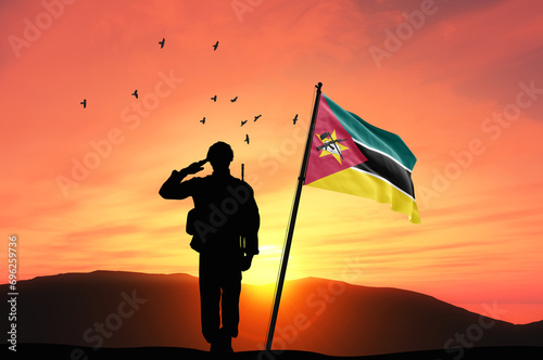 Silhouette of a soldier with the Mozambique flag stands against the background of a sunset or sunrise. Concept of national holidays. Commemoration Day. photo
