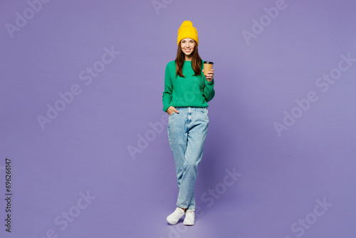 Full body young woman she wears green sweater yellow hat casual clothes hold takeaway delivery craft paper brown cup coffee to go isolated on plain pastel light purple background. Lifestyle concept.