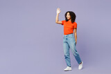 Full body side view smiling fun little kid teen girl of African American ethnicity wear orange t-shirt walk go wave hand isolated on plain pastel purple background studio. Childhood lifestyle concept.