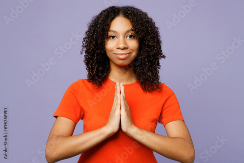 Little kid teen girl of African American ethnicity wear orange t-shirt hold hands folded in prayer gesture, begging isolated on plain pastel light purple background studio Childhood lifestyle concept photo