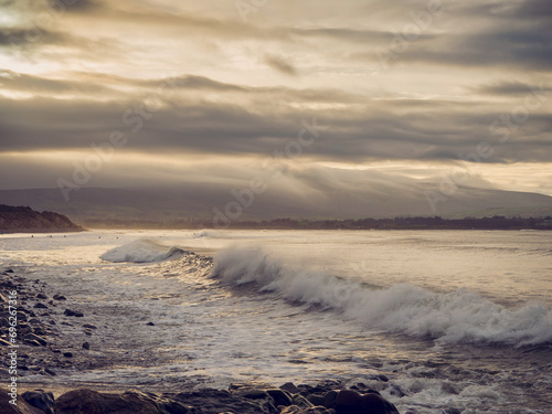 Powerful wave hit rough stone beach, mountains and dramatic cloudy sky in the background. Calm sunset time. Strandhill beach, Sligo, Ireland. Popular travel destination with waves and stunning nature