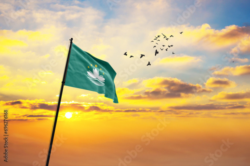 Waving flag of Macao against the background of a sunset or sunrise. Macao flag for Independence Day. The symbol of the state on wavy fabric.