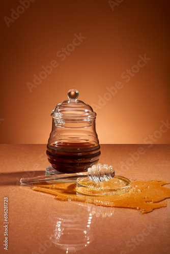 Front view of a glass jar containing honey, honey scattered on a brown background with glassware. Honey can be made into medicine to heal wounds. photo