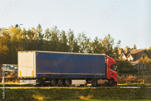 A red truck transports goods across a picturesque landscape illuminated by the golden hue of the setting sun. Truck transportation.