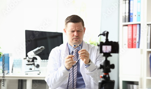 Portrait of serious blogger looking attentively at stethoscope. Handsome doctor recording video for vlog in modern office for internet channel. Blogging concept