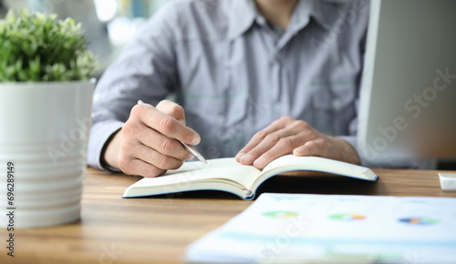 Businessman sits at a table holds pen in his hands and writes in notebook. Business education concept