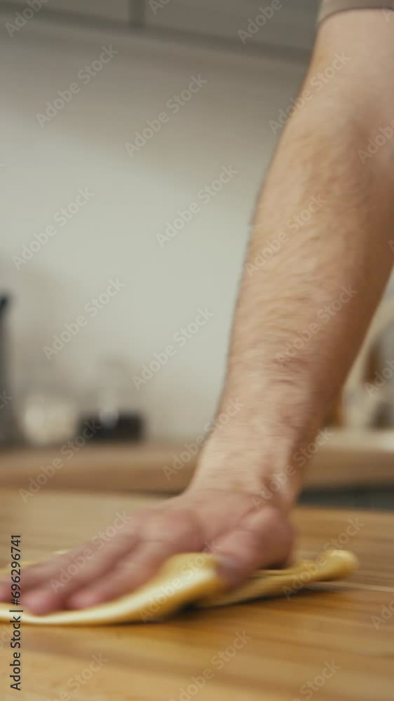 Vertical stab shot of unrecognizable male hand wiping or cleaning dinner table with cloth after meal in modern kithcen