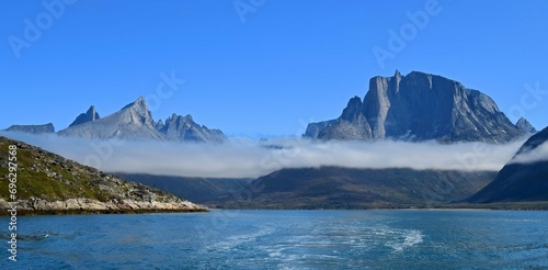 rugged mountain peaks and low-lying clouds near the sermeq glacier at the end of the tasermuit fjord on a sunny summer day near nanortalik, in southern greenland