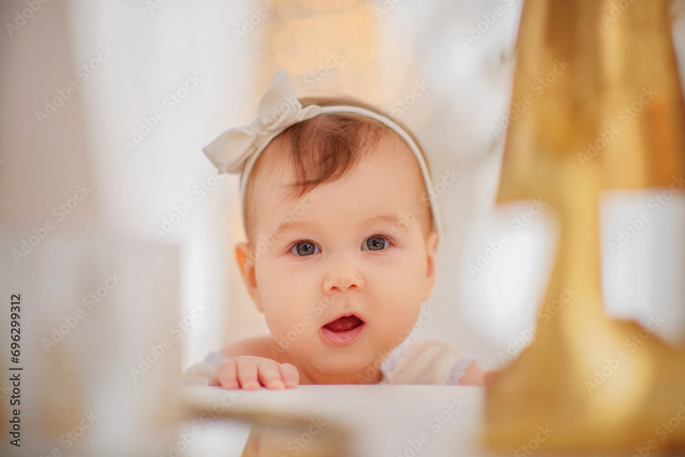Little beautiful girl in a bodysuit. New Year. Christmas. The girl smiles. Decorated Christmas tree. Girl with a bow. Portrait. Winter. Lights in the background. The baby is playing. Little beautiful girl in a bodysuit. New Year. Christmas. The girl smiles. Decorated Christmas tree. Girl with a bow. Portrait. Winter. Lights in the background. The baby is playing.