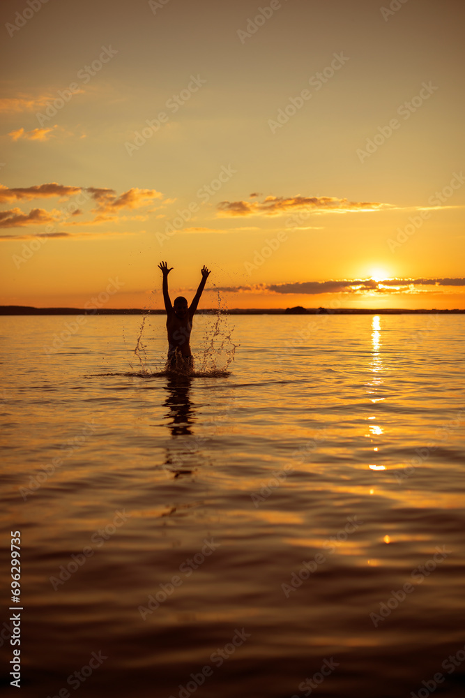 silhouette of a man in the water against the backdrop of the summer orange sunset sun. A joyful summer holiday on the water
