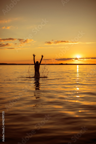 silhouette of a man in the water against the backdrop of the summer orange sunset sun. A joyful summer holiday on the water

