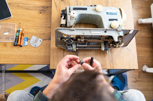 Repairman master is testing old disassembles sewing machine in workshop repairing it sitting at table, side view. Man is looking inside sewing machine trying to repair it, hands closeup. photo