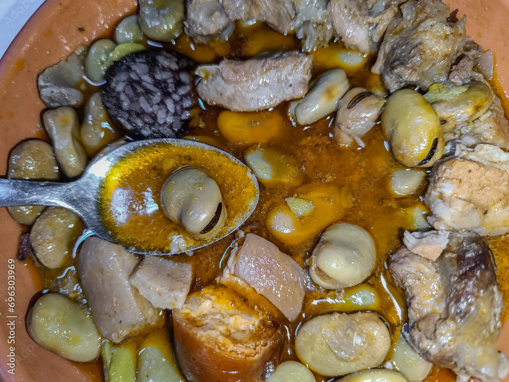 Spoon with broad beans in sauce on a plate of typical broad beans with pork ribs and sausages Spoon with broad beans in sauce on a plate of typical broad beans with pork ribs and sausages