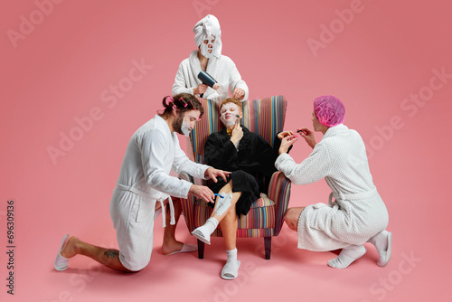 Friends support and care. Men in face masks, doing nails, depilation, taking care after skin against pink background. Concept of leisure activity, fun, bachelor party, friendship, spa, cosmetology photo