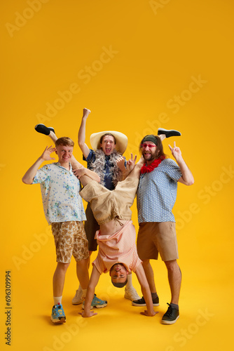 Emotional happy young men, friends in stylish clothes having fun together, relaxing, dancing on summer vacation against yellow background. Concept of leisure, emotions, friendship, fun, bachelor party photo