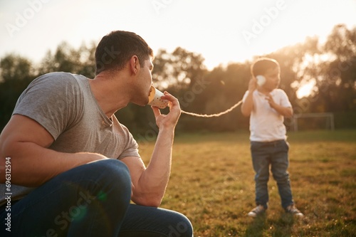 Talking by using string can phone. Father and little son are playing and having fun outdoors photo