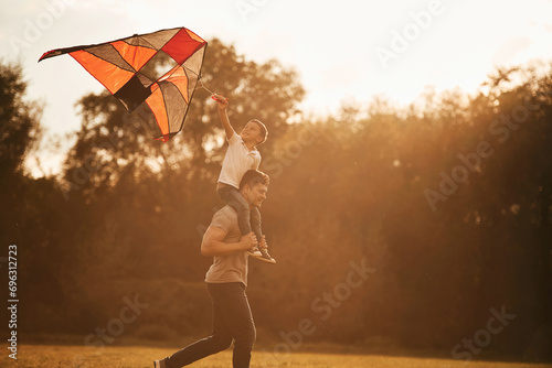 Red colored kite in hands. Father and little son are playing and having fun outdoors #696312723