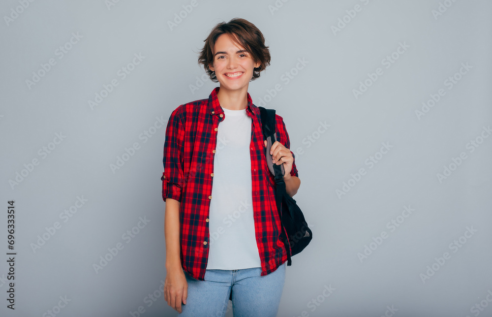 Beautiful, young, smart and stylish student girl with short hair smiling with a backpack on her shoulders looking at the camera. University, beginning, school, education, college, classes.