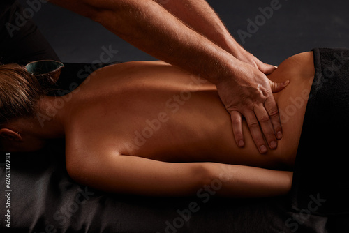 handsome male masseur giving massage to girl on black background  concept of therapeutic relaxing massage