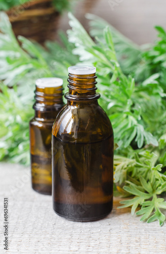 Small bottle with essential wormwood oil (extract, tincture, infusion). Old wooden background. Aromatherapy, spa and herbal medicine concept.