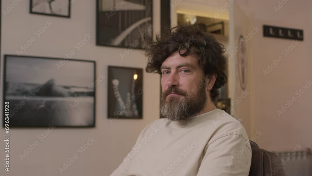 Medium arc shot of bearded man with messy hair sitting in barbershop and looking at camera Medium arc shot of bearded man with messy hair sitting in barbershop and looking at camera